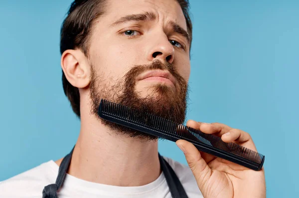 Retrato de un peluquero en un delantal sobre un peinado de fondo azul modelo peine tijeras — Foto de Stock