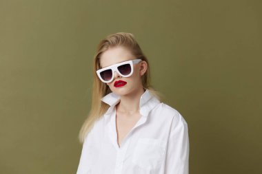 Sarışın, beyaz gömlekli, güneş gözlüklü bir kadın.