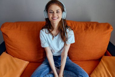 Portakal rengi koltukta değişmeden kulaklıkla müzik dinleyen bir kadının portresi.