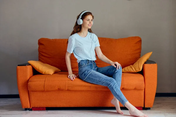 Mulher alegre sentado no sofá em casa ouvir música em tecnologias de fones de ouvido — Fotografia de Stock