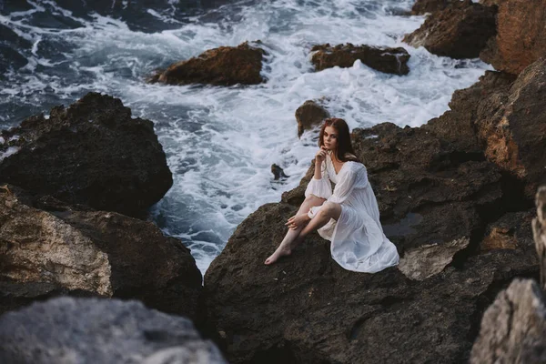 Barefoot woman in white dress sits on a stone with wet hair — Stock Photo, Image