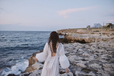 red-haired woman in white dress walking along the coast of the ocean rocks unaltered