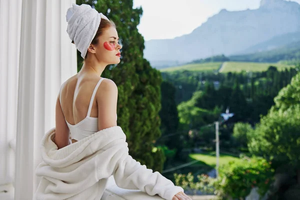 Attractive young woman in a robe stands on an open balcony looking on the view — Foto Stock