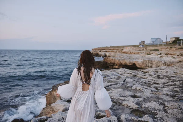 Mujer pelirroja vestida de blanco caminando por la costa del océano rocas inalteradas —  Fotos de Stock