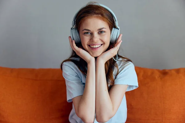 Bela mulher no sofá laranja ouvindo música com fones de ouvido inalterados — Fotografia de Stock