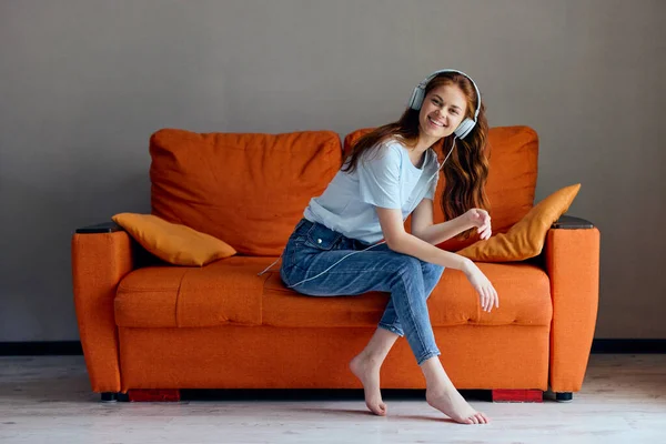 Bela mulher no sofá laranja ouvindo música com tecnologias de fones de ouvido — Fotografia de Stock