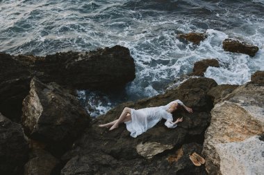 Beautiful bride Lies on his back on a stone cliff, cloudy weather view from above
