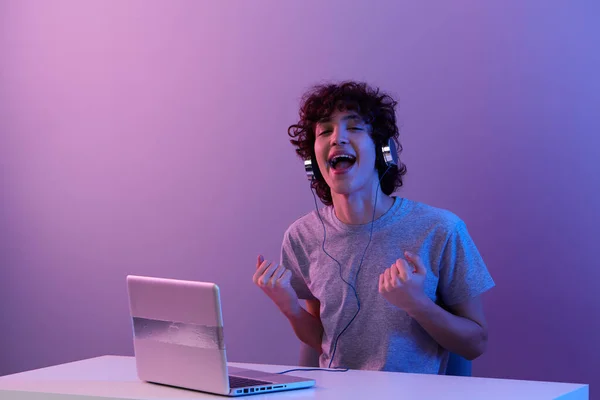 Gamer in headphones in front of laptop entertainment violet background — Photo
