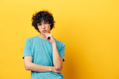 Mavi tişörtlü kıvırcık saçlı dalgın bakışlı bir adam.