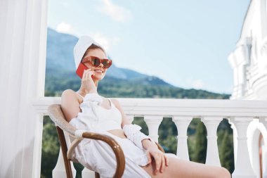 Balkonda oturan kırmızı cep telefonlu genç bir kadının portresi değiştirilmemiş.