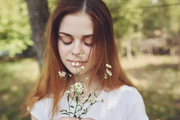 Donna in t-shirt bianca con fiori di campo sulla sua mano sulla natura in un prato — Foto Stock