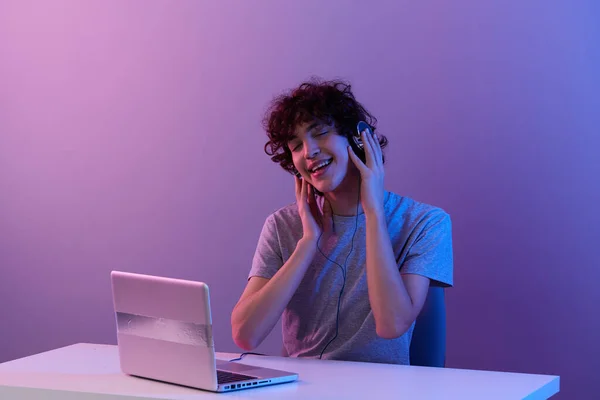 Gars cyberespace jouer avec des écouteurs devant un ordinateur portable fond violet — Photo