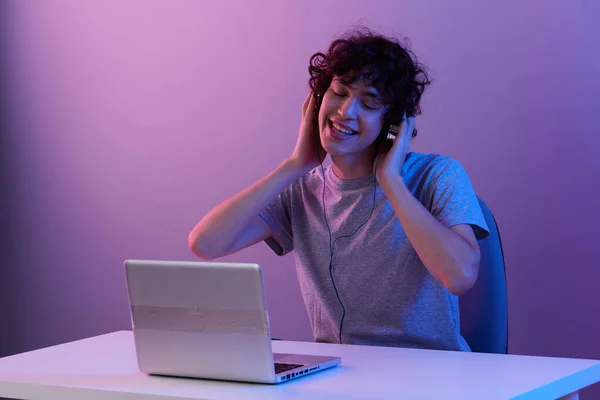 Man cyberspace playing with headphones in front of a laptop violet background — Photo