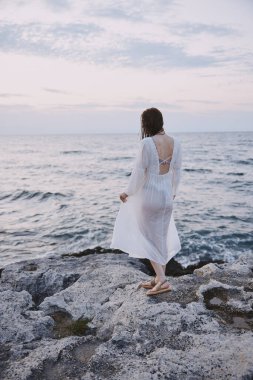 Kadın okyanus taşlarının kıyısında duruyor.