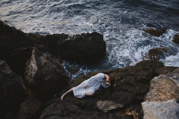 Beautiful young woman in a secluded spot on a wild rocky coast in a white dress Summer vacation concept — 图库照片