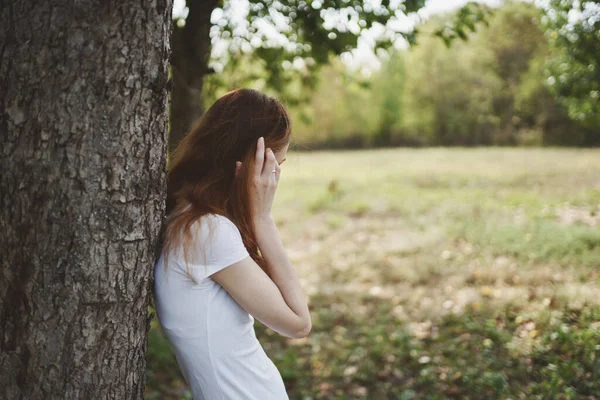 Bonita camiseta de mujer se encuentra cerca de un árbol en la naturaleza en un campo —  Fotos de Stock