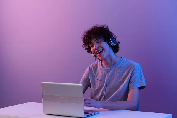 Chlap kyberprostor hrát se sluchátky v přední části notebooku fialové pozadí — Stock fotografie