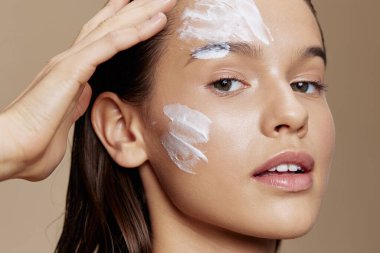 young woman with moisturizer on the cheeks in the eye area on  beige background. High quality photo