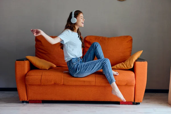 ヘッドフォンで音楽を聴くオレンジのソファの上の女性ライフスタイル — ストック写真