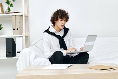 Dizüstü bilgisayarın oturma odasının önündeki masada oturan kıvırcık adam.