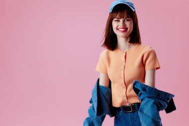 Şapka ve kot ceketli güzel, modaya uygun bir kız pembe arka plan pozu veriyor.