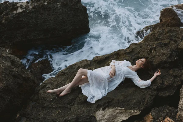 Mujer en vestido blanco largo cabello mojado acostado en un acantilado rocoso concepto de vacaciones — Foto de Stock