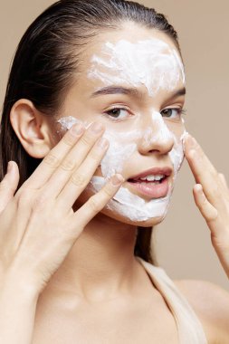 Kadın rahatlatıcı bir yüz maskesi takıyor. Kozmetik bej arka plan.