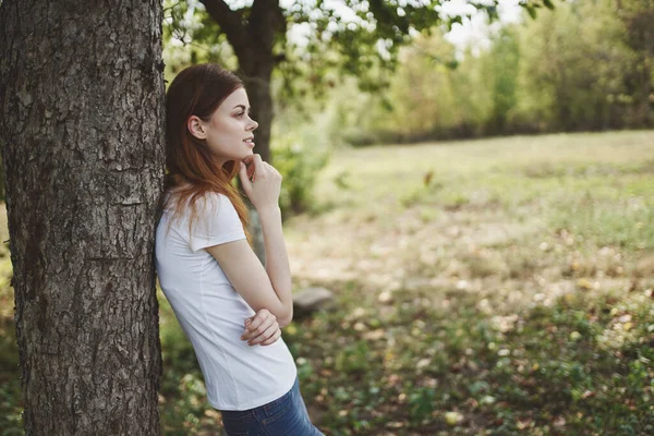 Hezká žena tričko stojí v blízkosti stromu v přírodě na poli — Stock fotografie