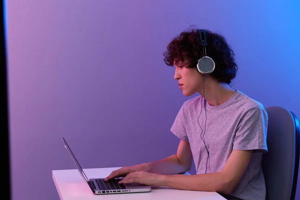 Cara encaracolado em fones de ouvido na frente de laptop entretenimento violeta fundo — Fotografia de Stock