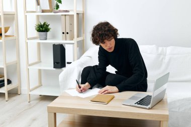 Dizüstü bilgisayarın oturma odasının önündeki masada oturan kıvırcık adam.