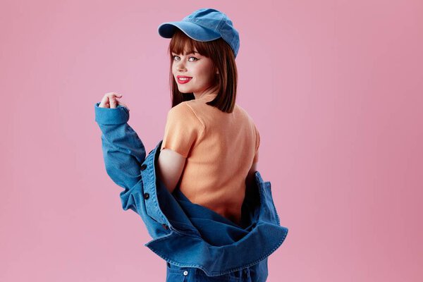 Positive young woman in a cap and denim jacket posing pink background unaltered