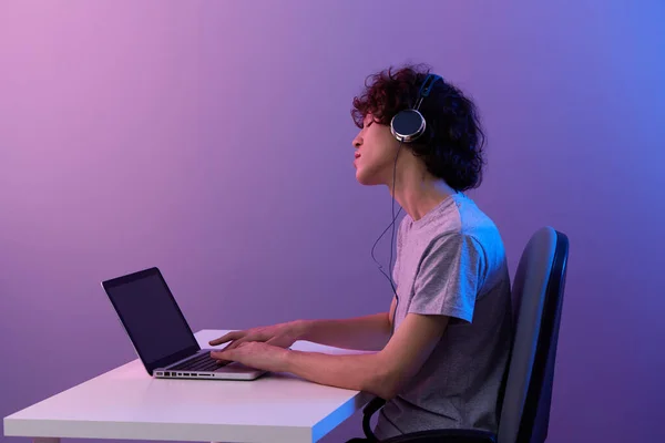 Gamer sentado na mesa de jogos laptop violeta fundo — Fotografia de Stock