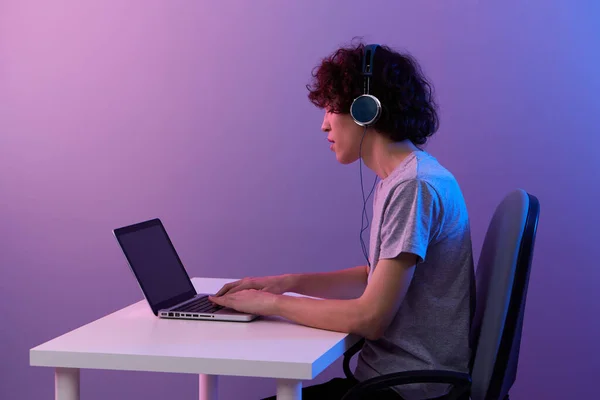 Homme dans les écouteurs devant ordinateur portable divertissement fond violet — Photo