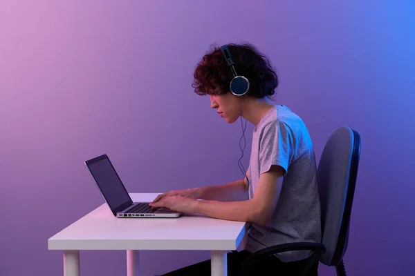 Σγουρός τύπος στα ακουστικά μπροστά από το laptop ψυχαγωγία βιολετί φόντο — Φωτογραφία Αρχείου