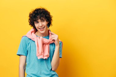 Mavi tişörtlü, pembe ceketli, sarı arka planlı bir adam.