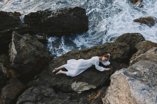 Attractive woman with long hair in long white dress wet hair lying on a rocky cliff unaltered — Stock Photo, Image