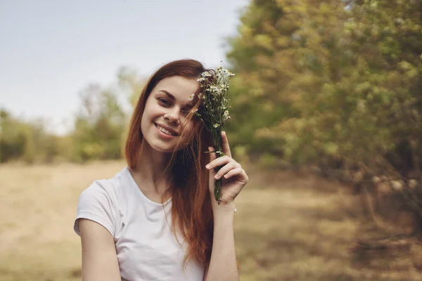 Frau mit weißen Blumen in der Hand ruht auf Feld und Bäumen Im Hintergrund der Lebensstil — Stockfoto