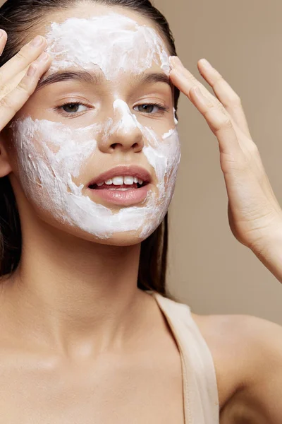 Mosolygós fiatal nő krém arcon pózol kozmetikumok tiszta bőr bézs háttér — Stock Fotó