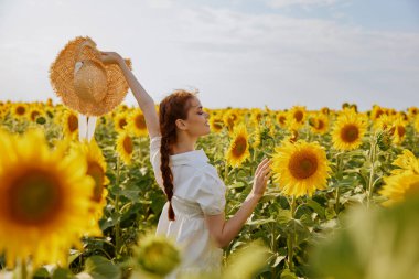 At kuyruklu neşeli kadın, elinde şapka, ayçiçeği tarlası doğası.