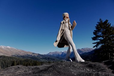 Sonbahar giysileri içinde bir kadın bir kayanın üzerinde duruyor mavi gökyüzü yaşam tarzı
