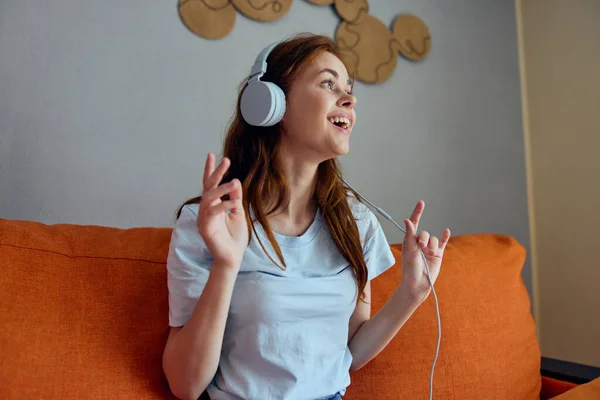 Bonita mulher ouvindo música com fones de ouvido no sofá laranja apartamentos — Fotografia de Stock