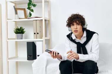 Kulaklıklı, telefonda internet bağlantısı olan, koltuktaki kıvırcık saçlı adam.