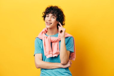 Mavi tişörtlü kıvırcık adam. Pembe ceketli, sarı arka planlı.