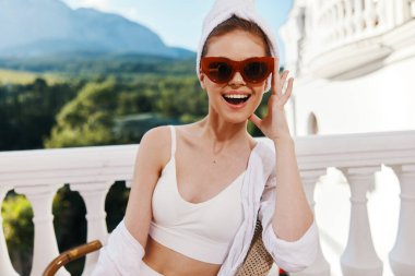 Güneş gözlüklü muhteşem kadının portresi açık bir balkonda oturup manzaraya bakıyor.