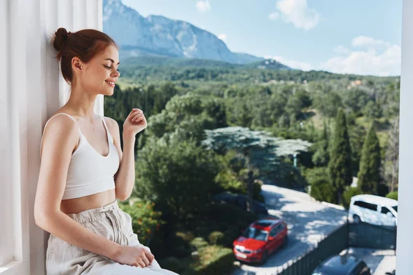 Attraente giovane donna ammira la vista sulle montagne sul balcone aperto dell'hotel Lifestyle — Foto Stock