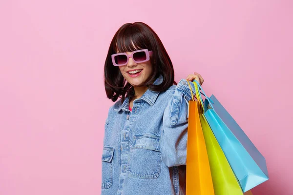 Mulher bonita em jaquetas jeans com sacos de compras coloridos fundo rosa — Fotografia de Stock