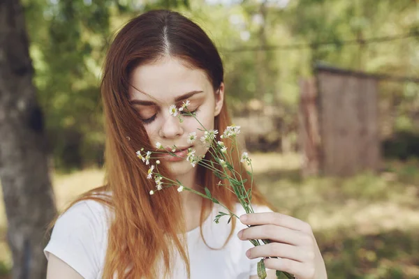 Kvinna i en vit t-shirt med vilda blommor på handen på naturen på en äng — Stockfoto