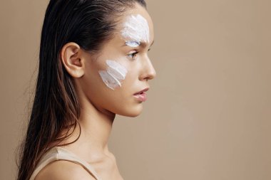 Güzel bir kadın bej arka planda rahatlatıcı bir yüz maskesi takıyor. Yüksek kalite fotoğraf