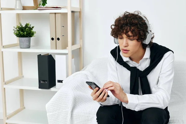 guy with curly hair sits on the couch wearing headphones on the phone