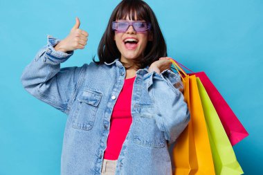 Renkli alışveriş çantaları olan kot ceketli kadın portresi.